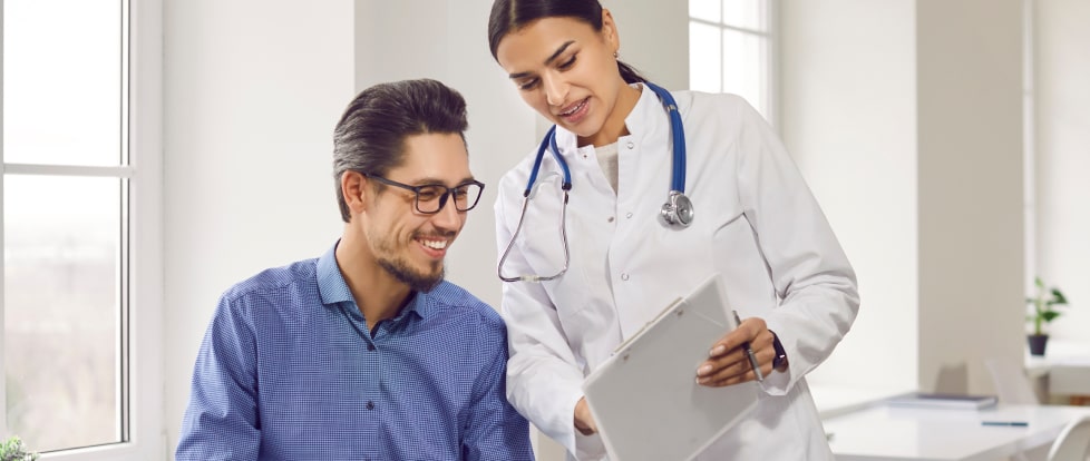 A doctor and a patient smiling and discussing medical results on a clipboard in a bright office.