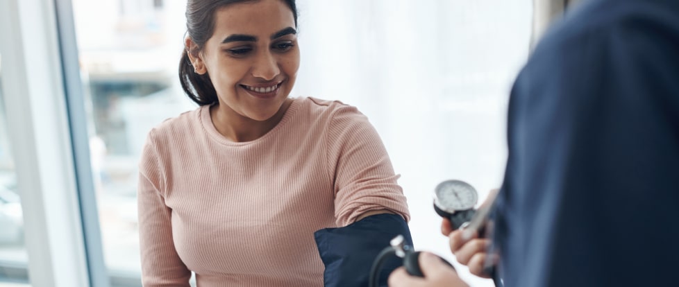 A woman smiles as a healthcare professional measures her blood pressure in a medical office.