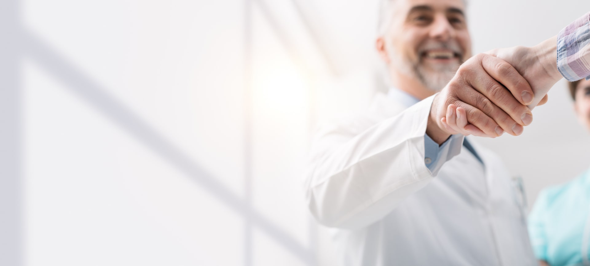 Close-up of a handshake between a smiling doctor in a white coat and a person in a plaid shirt.